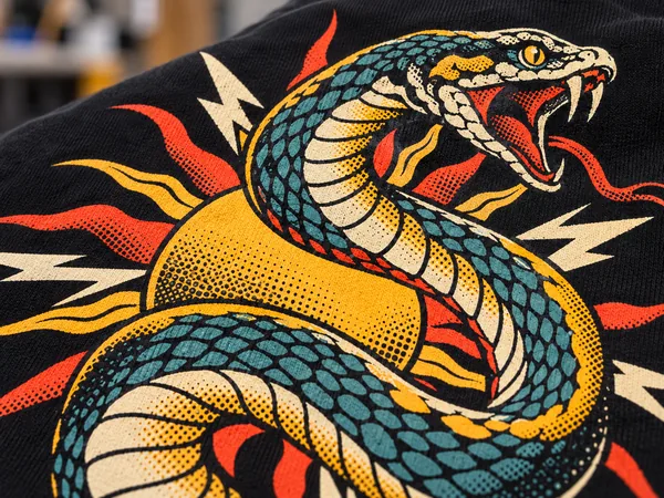 Detailaufnahme eines Siebdruck-Motivs mit Schlange im Tattoo-Stil auf schwarzem Stoff