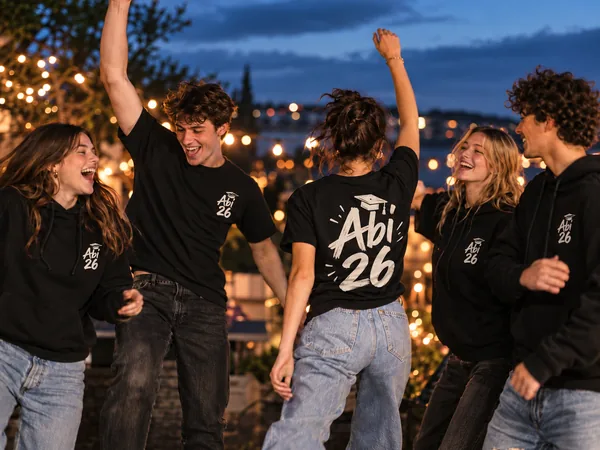 Gruppe feiernder Abiturientinnen und Abiturienten in schwarzen Hoodies und T-Shirts mit Abi-26-Aufdruck